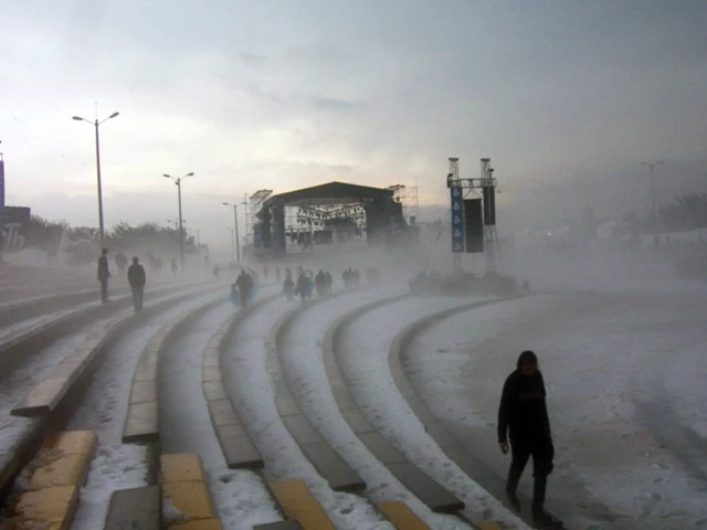 Personas caminan entre graderías cubiertas de granizo frente a un escenario
