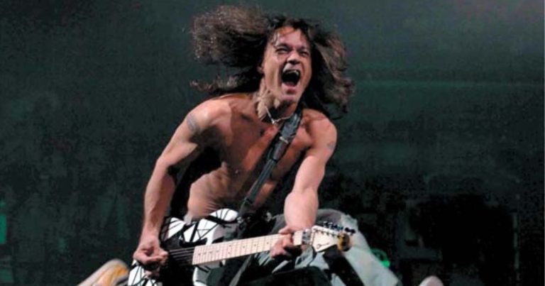 Eddie Van Halen gritando mientras toca su guitarra blanca con rayas negras durante un concierto