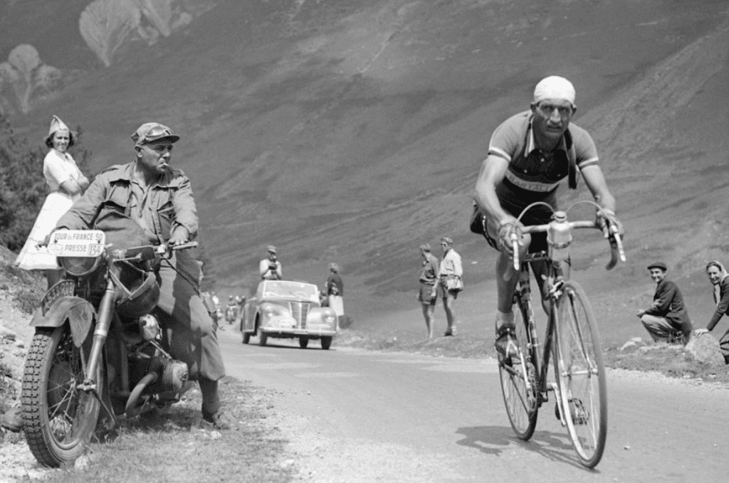 Gino Bartali pedaleando en su bicicleta por una carretera, en una fotografía en blanco y negro tomada durante la década de 1940.