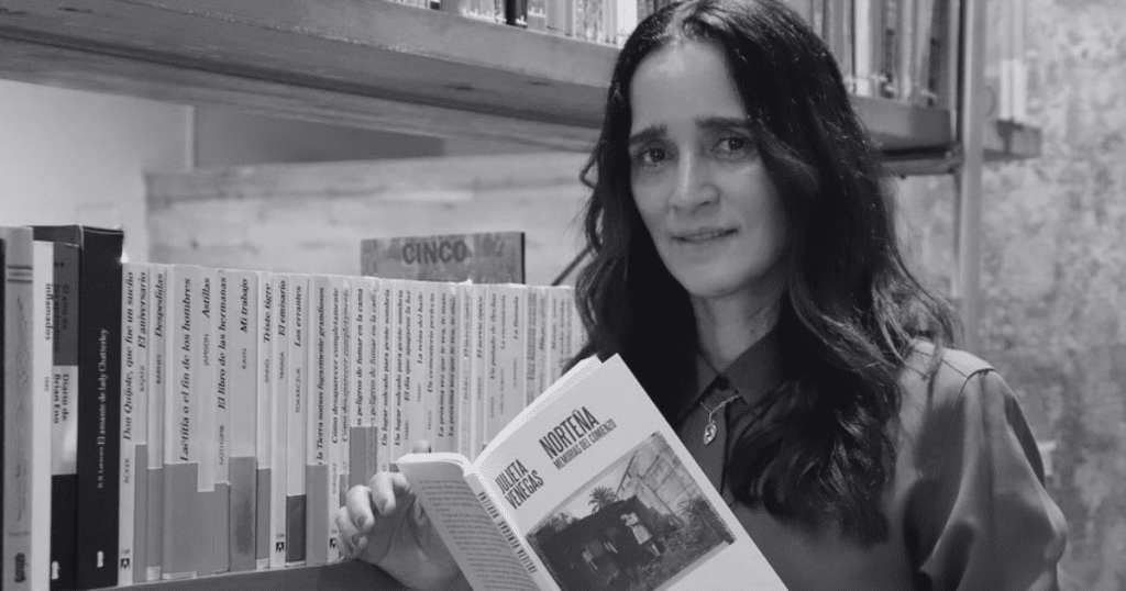 Julieta Venegas sostiene Norteña. Memorias del comienzo, su primer libro, frente a una estantería, en una imagen en blanco y negro.