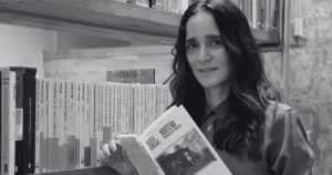 Julieta Venegas sostiene Norteña. Memorias del comienzo, su primer libro, frente a una estantería, en una imagen en blanco y negro.