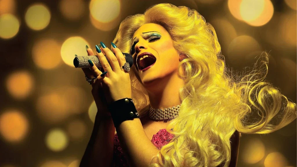 Hedwig, cantante de rock con peluca rubia y maquillaje brillante, cantando al micrófono en 'Hedwig and the Angry Inch'