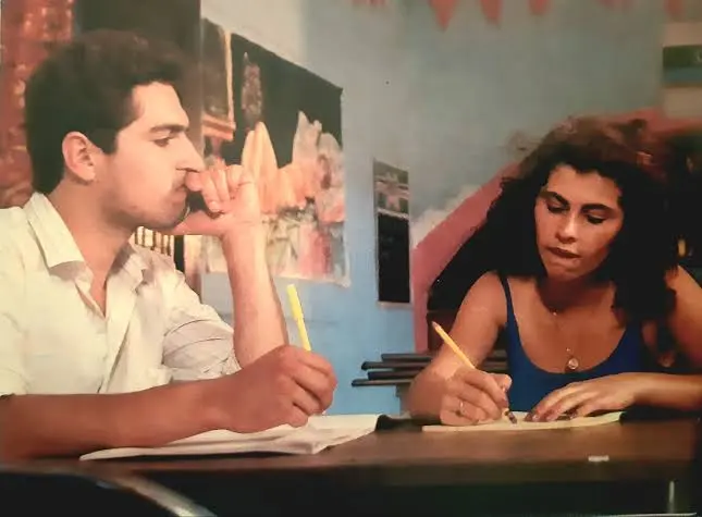 Carlos Duplat: escena de “Fronteras del regreso” con dos jóvenes escribiendo en una mesa, ambiente de aula y tono realista