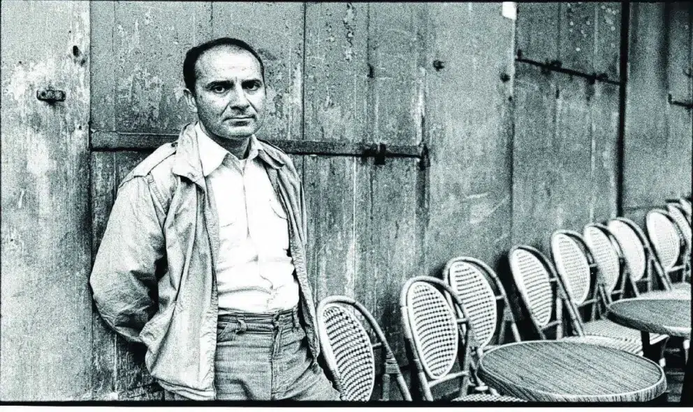 Manuel Puig de pie junto a una terraza vacía, retrato en blanco y negro