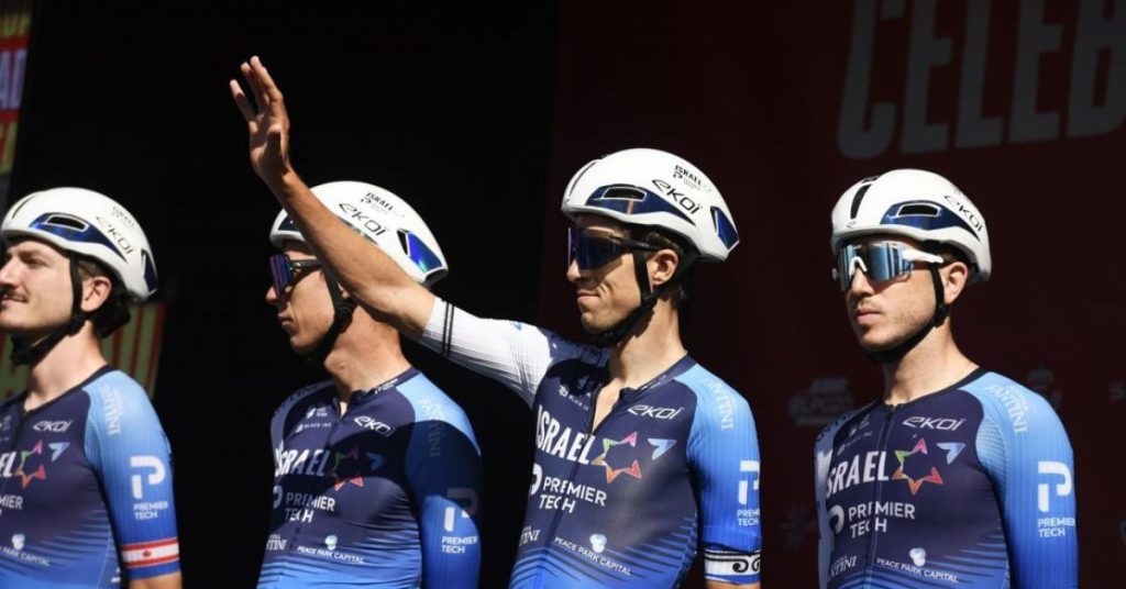 Ciclistas del Israel Premier Tech alineados antes de la salida; uno saluda al público durante la Vuelta a España 2025.