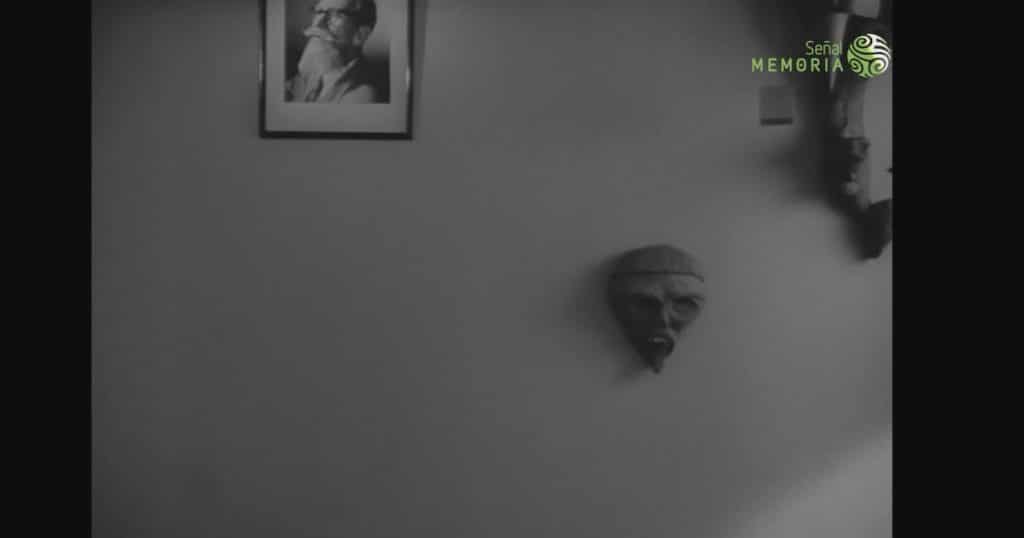 Pared interior con un retrato enmarcado y dos máscaras, en una escena en blanco y negro de La frontera del sueño.