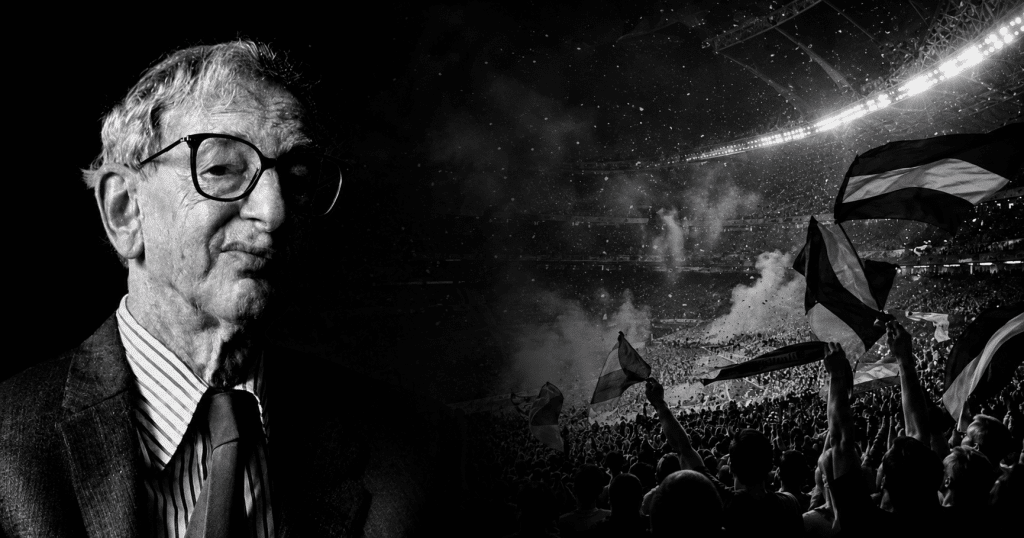 Retrato en blanco y negro de Eric Hobsbawm junto a una tribuna llena de hinchas con banderas en un estadio, en una imagen sobre fútbol, nación e identidad colectiva.