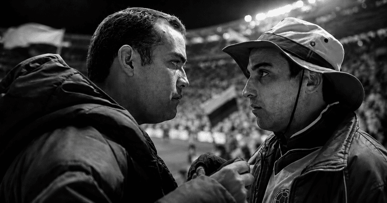 Mariano Concha y Saúl, protagonistas de La pena máxima, se enfrentan en primer plano dentro de un estadio lleno, en una imagen en blanco y negro con ambiente de fútbol colombiano.