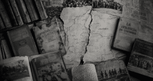 Mapa de Colombia rasgado rodeado de libros antiguos, periódicos y fotografías de archivo sobre la violencia política en Colombia.