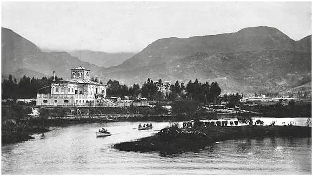 Fotografía antigua en blanco y negro del parque Luna Park en Bogotá, con laguna, botes y el edificio principal con torre reloj