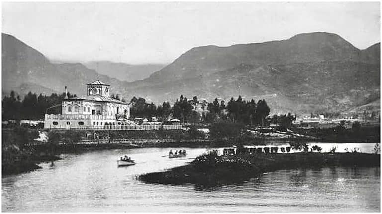 Fotografía antigua en blanco y negro del parque Luna Park en Bogotá, con laguna, botes y el edificio principal con torre reloj