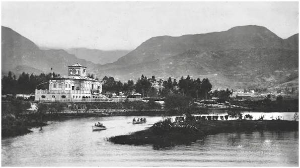 Fotografía antigua en blanco y negro del parque Luna Park en Bogotá, con laguna, botes y el edificio principal con torre reloj