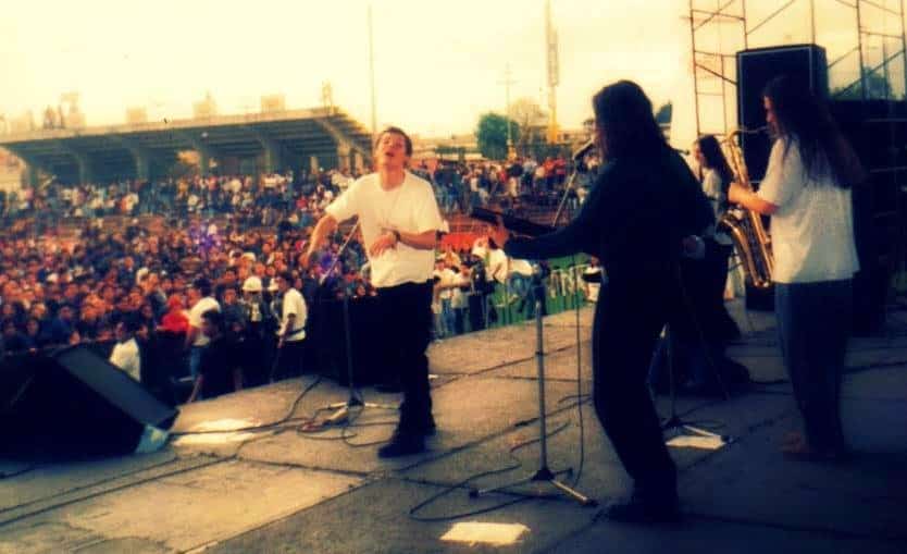 Texto alternativo: Integrantes de Morfonía sobre la tarima de Rock al Parque, con el cantante al frente con camiseta blanca y un saxofonista a la derecha, ante un público numeroso frente a una tribuna.